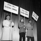 Arbogarevyns medlemmar spelar upp sin Jubileumsrevy. Tre personer på scenen, alla i ytterkläder, bär var sitt plakat.