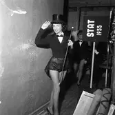 Arbogarevyns medlemmar spelar upp sin Jubileumsrevy. Här är flickorna på väg upp på scenen, iklädda korta frackar och höga hattar. Nummer två är Gullan Kästämä.