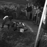 Arbogas Stjärnknutte
Tävling i terrängkörning med motorcykel. En man har kört omkull. Publiken står alldeles intill banan.