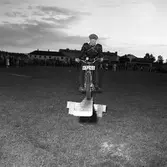 Arbogas Stjärnknutte
tävling. Balansövning med motorcykel på lutande bräda
Bilden ser ut att vara tagen på en fotbollsplan, på kvällen. En stor publik tittar på.