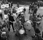 Artister i Scalarevyn går i parad på Nygatan. Trumspelare och skyltbärare. Efter gatan står människor och tittar på.
Den högra mannen, i fotbollskläder, är vår lokale revyspelare Larz-Thure Ljungdahl.
Se även bild och text, AKF-01222
En bild, från detta tillfälle, finns med i Reinhold Carlssons bok 