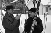 Skidtävlingen AT-loppet.
Till vänster, med kameran, Lennart Pettersson (kallad Svarten), till höger, med skidorna, Torsten Eriksson. Båda männen bor i Medåker.
(AT kan betyda Arboga Tidning)
I bakgrunden ses ett hus.