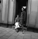 Ateljé Touché. Marianne Rosenqvist (sittande) och Britt-Marie Utterström (stående).
Två kvinnor som visar mode. Marianne är klädd i blus och kjol. Britt-Marie har en dräktjacka och kjol i samma tyg.
De drev ateljén tillsammans.