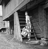 Ateljé Touche. Marianne Rosenqvist visar mode; hellång klänning med bar rygg och långa handskar.
Bilden är tagen vid gamla timmerhus på Ahllöfsgatan.
