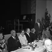Tal hålls för Axel Karlsson, Medåker. (Axel är den andre mannen från höger).
Uppklädda människor vid dukat bord. Blombukett i vas. På scenen står ett piano.
Bilden kan vara tagen i Medåkers bygdegård.