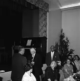 Axel Karlsson, Medåker (mannen i mitten) får en gåva.
Uppklädda människor vid dukat bord. Blommor i vas. På scenen, bakom människorna, står ett piano.
Bilden är möjligen tagen i Medåkers bygdegård.