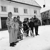 Barn med julklappar. Två flickor visar nya käder. En pojke med en mini-cykel. Flickan längst till höger har en hund i famnen.