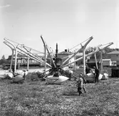 Barnens Dag. Två män arbetar med en karusellkorg. Två små pojkar tittar på. Karusellen verkar tillfälligt placerad. Platsen kan möjligtvis vara vid Vallgatan. I bakgrunden skymtar tornet på Heliga Trefaldighets Kyrka.