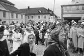 Barnens Dag firas med en parad av utklädda barn. De kommer från Västerlånggatan och svänger upp mot Kapellgatan. En stor publik möter dem på torget. De två kvinnorna, längst till höger, bär Barnens-Dags-blomma på kappslaget.
I bakgrunden ses Sture Möbler, Motorfirman Henry Molin och Sturebion.