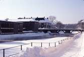 Biblioteket, Kapellbron och Labron/Ladbron i snö.
Is och snö på Arbogaån. Två personer står nedanför trappan, från Kapellgatan, och matar änder i ån.