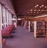 Interiör från biblioteket på Kapellgatan. Sittplatser till vänster, vid fönstren, och bokhyllor tillhöger. Heltäckande matta.