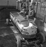 Björkmans Nöjesfält. Bröderna John och Martin Björkman vid ett karuselltåg som just lastas av en riktig järnvägsvagn. Det lilla loket ska användas på deras tivoli.