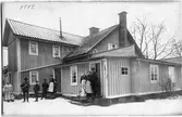 Bostadshus vid Arboga Mekaniska Verkstad. Familjerna står utanför huset. En man håller en hund i famnen. Det är vinter och snö.
AMV