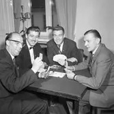 Distriktsmästerskap i bridge
Fyra män sitter vid ett bord och spelar kort. I fönstret står en ljusstake.
Bridge-DM