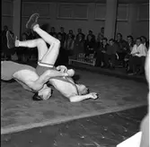 Brottning. Arboga AK tävlar mot Sala. Två brottare på mattan. Publiken på bänkar efter väggen.
Arboga AtletKlubb