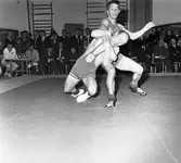 Tävlingen Fyrstadsbrottningen. Deltagande städer: Arboga, Eslöv, Uddevalla och Falkenberg.
Två män på brottarmattan. Publik i gymnastiksalen.
Arboga Atletklubb