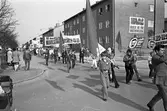 Demonstration på första maj. Människor tågar med plakat, fanor och banderoller.
Förstamajtåg.