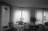 Interiör från bostad i kvarteret Tullnären, mellan Storgatan - Trädgårdsgatan och Herrgårdsgatan - Paradisgränd.
I hörnet står en kakelugn. Framför fönstren står bord med krukväxter. Mellan de båda fönstren ses en radioapparat. Ovanpå den står en kruka (av koppar?) med tallris. Tre pinnstolar.
Fotografens anteckning: Dokumentation av fastigheter i kvarteren söder och norr om ån. Bilder och beskrivning finns på Arboga Museum.