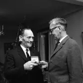 Einar Larsson i Hamre får en armbandsklocka.
En man tar emot en gåva av en annan man. I bakgrunden ses en julgran.