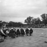 Musikkåren spelar vid invigningen av Ekbacksbadets utomhusbassäng! Publiken sitter på läktaren på andra sidan poolen. Hopptornet ses i bakgrunden.