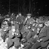 FBU-ungdomar övar i skogen. Det är vinter och snö. Grabbarna sitter på granris och äter ur sina plåtburkar. De är iklädda yllerockar och mössor med öronlappar. Några har båtmössor.
FBU betyder Frivillig befälsutbildning