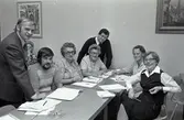 FCO-kurs. Flera personer sitter vid bord med papper framför sig. Mannen vid väggen är Torbjörn Harlin.