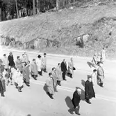 Första maj. Demonstrationståg. Herrar i hatt och överrock går i prydliga rader.
Andra raden, närmast kameran, är Nils Brodin.
En kvinna med två barn går utanför ledet.
