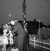 Konung Gustaf Vl Adolf gästar Arboga under sin Eriksgata. Här står han på en uppbyggd estrad, på Stora torget, och får en blombukett av en liten flicka. Bakom kungen står stadsfullmäktiges ordförande, Jonas Carlsson. 6000 personer är samlade för att se och höra kungen.
För värdskapet, under kungens besök, svarade stadsfullmäktiges ordförande Jonas Carlsson och kommunalborgmästare Danliel Ekelund. Den organisationskommitté som ansvarade för arrangemangen, hade hos drätselkammaren begärt en summa av 3000 kronor för att täcka kostnaderna vid kungabesöket. Beloppet beviljades. 
Tiden för kungens besök var beräknad till 130 minuter.