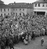 Plublik på Stora torget. Kung Gustaf Vl Adolf gästar Arboga under sin Eriksgata. I främsta ledet står Hemvärnet och Lottakåren. I bakgrunden ses Sture Möbler och Sture-Bion på var sida om infarten till Västerlånggatan.
För värdskapet svarade stadsfullmäktiges ordförande Jonas Carlsson och kommunalborgmästare Danliel Ekelund. Den organisationskommitté som ansvarade för arrangemangen, hade hos drätselkammaren begärt en summa av 3000 kronor för att täcka kostnaderna vid kungabesöket. Beloppet beviljades. 
Tiden för kungens besök var beräknad till 130 minuter.