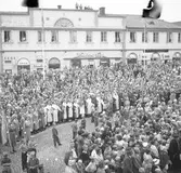 Människor har samlats, på Stora torget, för att se och höra kung Gustaf Vl Adolf. Han gästar Arboga under sin Eriksgata. I publiken ses Arboga Lottakår, kvinnor i folkdräkt, Arboga Scoutkår, gamla och unga. Några har klättrat upp på taket på Lungborgska fastigheten. I bakgrunden ses skoaffären, Strandbergs (Atchy Strandbergs frisersalong), Konditori Saga och Järnbolaget.
För värdskapet svarade stadsfullmäktiges ordförande Jonas Carlsson och kommunalborgmästare Danliel Ekelund. Den organisationskommitté som ansvarade för arrangemangen, hade hos drätselkammaren begärt en summa av 3000 kronor för att täcka kostnaderna vid kungabesöket. Beloppet beviljades. 
Tiden för kungens besök var beräknad till 130 minuter.