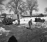 Arbetet med den nya skolan har börjat. En lastbil och män med maskiner och verktyg ska bygga Gäddgårdsskolan. Några barn tittar på.