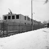 Gäddgårdsskolan byggs. Två män murar tegel på huvudbyggnaden.
Det är vinter och snö.