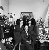 Byggmästare Johan Sörén med sina barn; Gustav, Allan, Lizzy och Ulla.
En man sitter i sin fåtölj i vardagsrummet omgiven av sina fyra, vuxna barn. Mannen har troligen fyllt år för vardagsrummet är fullt av blommor, i vaser, korgar och krukor.