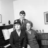 Flygvärdinna Katrin Zander är hemma på besök. Hon är iklädd sin uniform. Bredvid henne sitter mamma Nanna Zander. Mannen heter Tomas Tunberg.
I rummet finns ett piano och en bokhylla.