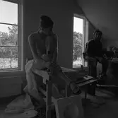 Keramikerparet Kerstin Hörnlund och Gösta Gräs i ateljén. Kerstin sitter på sitt arbetsbord. Nedanför henne ligger en gjutform. Gösta sitter på en hög pall. Genom fönstren ses ågårdar på södra sidan.
Läs Kerstins text 