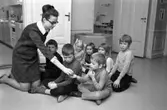 Fröken Marianne Astlid delar ut vitaminpiller till barnen på lekskolan Sörgården, avdelningen Humlan.
Barnen är, främsta raden, från vänster: okänd, Mikael Köld och Thomas Andersson.
Andra raden, från vänster: Kristina Andersson, Carina Bertilsson (