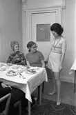 TBV ordnar modevisning och bjuder på kaffe och landgång. Vid bordet sitter Ann-Marie Törnqvist (blond) och Gulli Hammarlund (mörk) och studerar mannekängens jumper och kjol.
Eftersom Sture Melander ses på en bild i sammanhanget, kan man gissa att kläderna kommer från Öhrman & Melander.