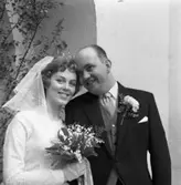 Margareta Einarsson och Rune Ström har gift sig i Heliga Trefaldighetskyrkan. Här ses brudparet vid den lövade kyrkporten. Bruden bär slöja, krona och handskar. Brudbuketten består av liljekonvaljer. Brudgummen har en nejlika på frackslaget.
Porträtt.