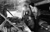 Familj grillar korv vid Maxelmossens vindskydd. Mamman bär ryssmössa. Det är vinter och snö.
Yngsta barnet har overall.