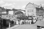 Riksdagens 550-årsjubileum firas i Arboga. På rådhusgården är en stor kupol uppspänd över en scen där en grupp spelar. Många människor har samlats.
En lastbil kör över Stora torget. På flaket står utklädda människor. I förgrunden ses lotteristånd.
Festligheterna pågår en vecka.