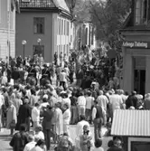 Allmänheten, en fanborg och ett stort pressuppbåd möter kungaparet som kommer gående på Rådhusgatan. Drottning Silvia har en blombukett i hänerna. Ridande poliser har kontroll. Dörren till Arboga Tidning står öppen. Heliga Trefaldighetskyrkan skymtar i bakgrunden.