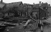 Rivning av en fastighet på Nygatan. Huset är en del av Glasbruksgården. Bräder och tjocka timmerstockar ligger på gården. Fruktträden står i bråten.
Byggnaden ligger i hörnet Östra Nygatan - Vikingagatan.