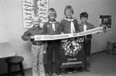 Scouter säljer majblommor. Fyra pojkar i scoutskjorta och sjal. De håller i en banderoll. Den tredje från vänster är Jens Gunnarsson.