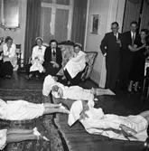 Spex på fest. Utklädda gummor gör gymnastik på golvet. Serveringspersonal och gäster ser på. I soffan sitter, utklädd till man, Greta Persson. I dörröppningen står Sten Wahlgren (som driver Boråsboden tillsammans med sin bror Stig) samt Folke Pettersson (som har musik-och pappershandel).
Platsen borde vara Stadskällaren eftersom Greta Perssons man, Gustav Adolf Persson, drev restaurangen.