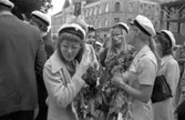Det är studentdag! Flickor med vita mössor och blombuketter om halsarna.
I bakgrunden ses 