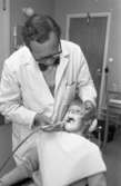 Tandläkare Sven Rosenbaum undersöker en ung patient.
Sven är klädd i skjorta, fluga och vit rock.