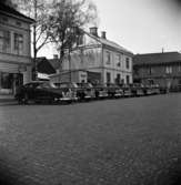 Taxi vid Järntorget. Tio svarta bilar är parkerade bredvid varandra. En fiskaffär, en bokhandel och Stenbäcks ses i bakgrunden.
