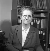 Telekommissarie Eva Geete/Eva Gethe på Televerket, Sohlénska huset, Nygatan.
Eva bär glasögon och har en brosch på slaget på dräktjackan. Bakom henne skymtar en skrivmaskin och en bokhylla.
Läs om Televerket och branden 1956 i Arboga Minnes årsbok 1993.
Porträtt.