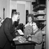 Sångaren Tore Skogman gästar Folkes Musik. Han står vid disken och talar med en ung flicka och en pojke. På disken står en kassaapparat och på väggen hänger en banjo. På hyllorna ligger instrumentfodral och noter samt en herrhatt.