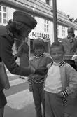 Trafikpropaganda. Bilkårist Britt-Marie Utterström delar ut höger-trafiks-märken. Här har en flicka och en pojke fått var sitt märke på jackan.
I bakgrunden ses Öhrman & Melanders klädaffär på Nygatan.